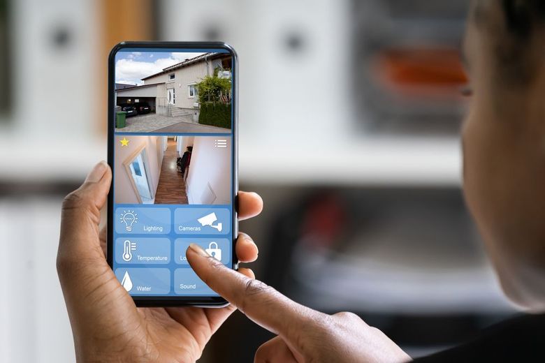 Hand holding a smartphone app for home security, showing live camera views and control buttons.