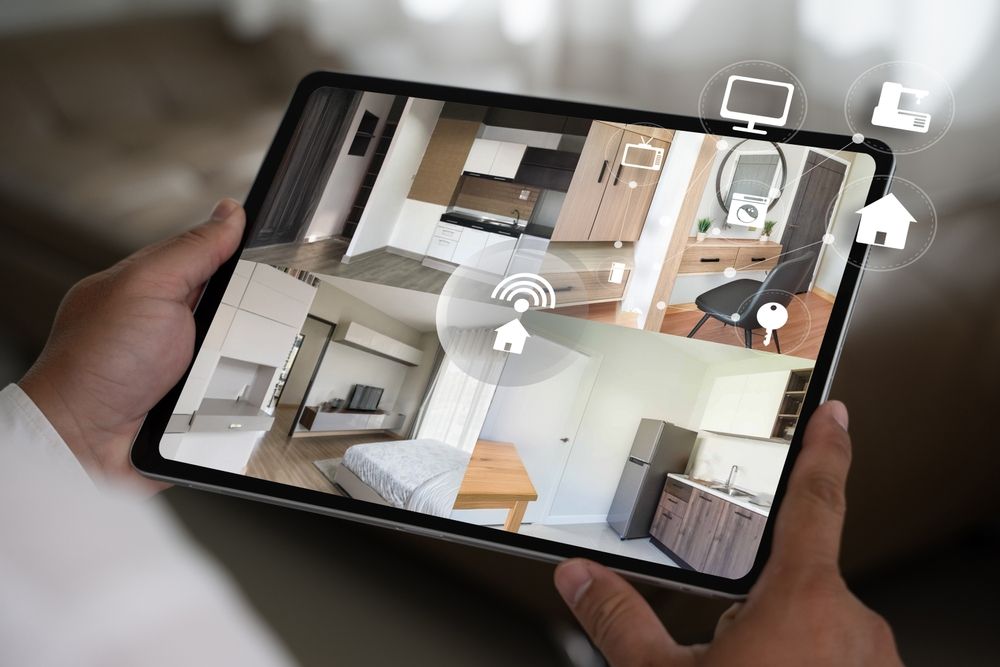 Hands holding a tablet displaying a home security camera app with multiple room views.