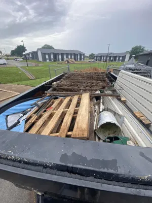 The bed of a truck is filled with debris, including wooden pallets, metal mesh, a white bucket, and other construction waste.