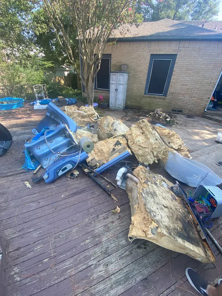 Damaged pieces of blue playground equipment and yellow foam debris scattered on a wooden deck in a backyard.