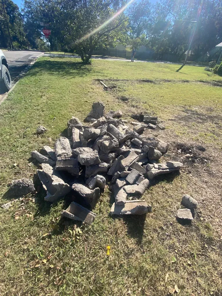 A pile of broken concrete chunks sitting on a patch of grass next to a residential street.