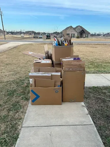 Several stacked cardboard boxes sit on a suburban sidewalk awaiting disposal or pickup.
