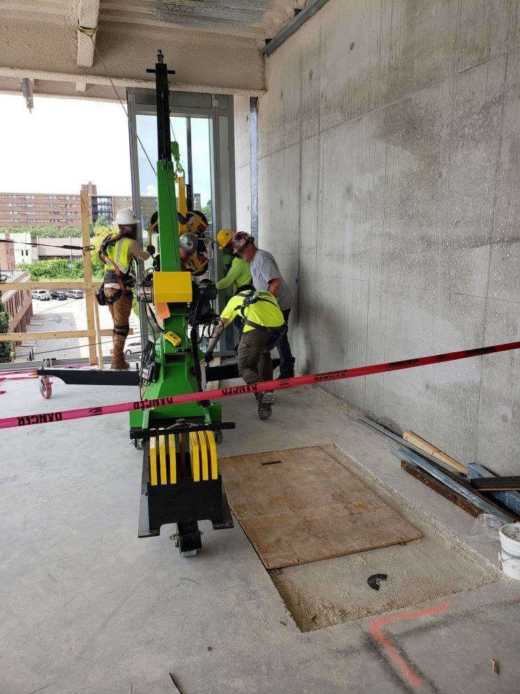 Construction workers in neon vests operate a green drilling rig inside a concrete building under construction