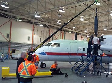 Workers servicing a small jet in a hangar, with one person on scaffolding near the cockpit.