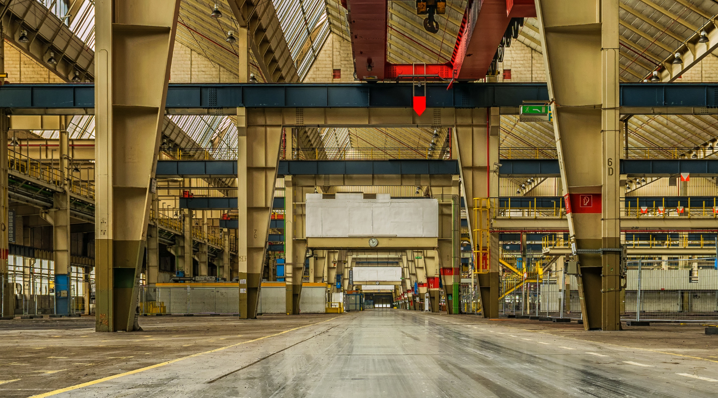Empty industrial warehouse interior with steel columns, overhead cranes, and a wide concrete floor