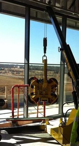 MicroCranes® mini crane. A mini crane hoist used in construction. Compact design, safely lifts up to 2,000 pounds. Yellow industrial lifting clamp hanging in front of large windows inside a warehouse or workshop