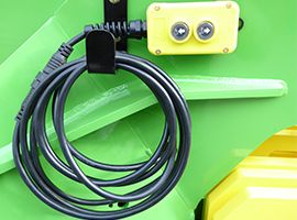 Coiled black cable with clip on green machine, beside a small yellow box with two lights
