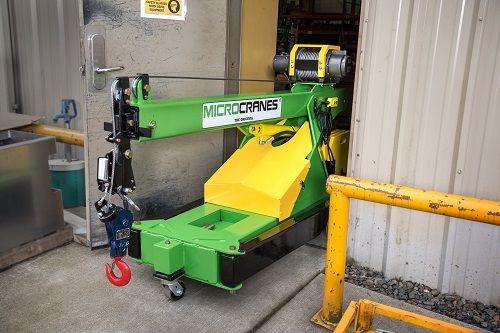 Green and yellow industrial machine in a workshop bay with a red wheel and yellow guardrail