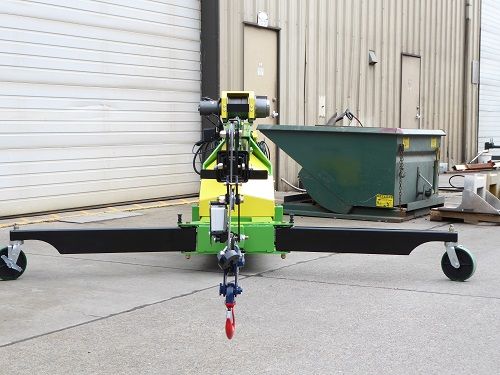 Small green-and-black wheeled lift machine outdoors beside a warehouse door and dumpster.