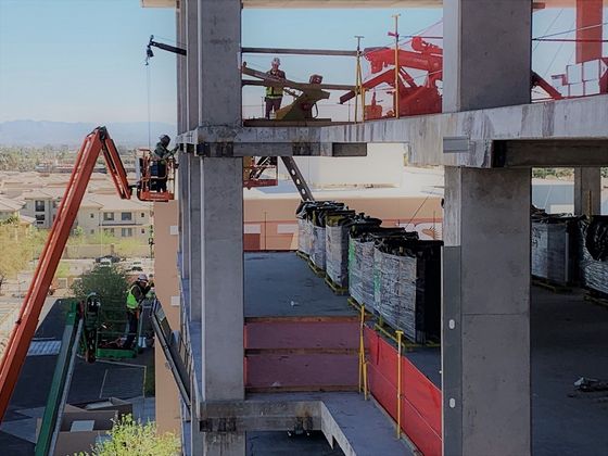 MicroCranes® mini crane. A mini crane hoist used in multi floor construction projects. Safely lifts up to 2,000 pounds. Construction workers on a concrete building frame, with cranes and red safety netting nearby.