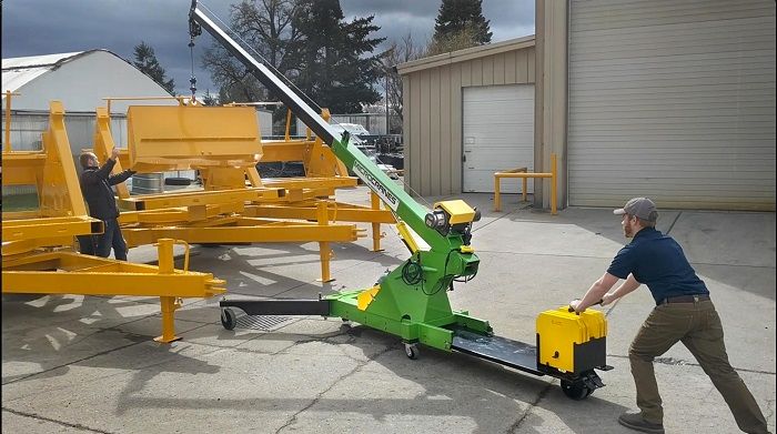 Man pushing a yellow tow bar to move a large orange machine in an outdoor industrial yard