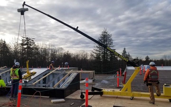 Workers guide a crane lifting a large ramp section at a roadside construction site.