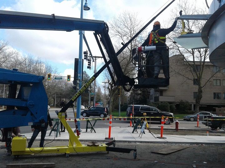 Utility workers operating a blue bucket lift beside a street with traffic cones and a damaged tree