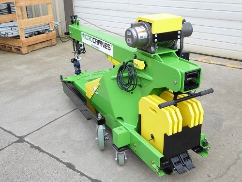 Green and yellow industrial machine on wheels parked outside a building.