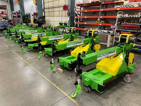 MicroCranes® Model M1 mini crane M1. A mini crane hoist used in many industries. Battery powered, lifts up to 2,000 pounds. Rows of green industrial machines with yellow parts lined up in a warehouse aisle.