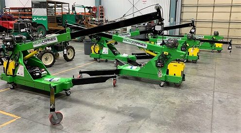 Green agricultural machinery with long booms displayed in a warehouse showroom