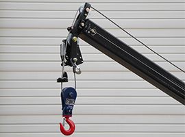 Crane boom with a blue lifting hook hanging in front of a white garage door