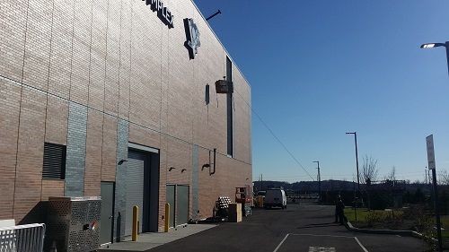 Brick industrial building with loading doors and a paved driveway under a clear blue sky