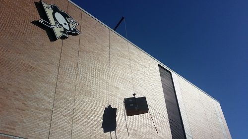 Sunlit brick building wall with mounted fixtures and a small sign against a clear blue sky