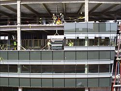Workers on a building facade installation, with a crane and exposed concrete structure above.