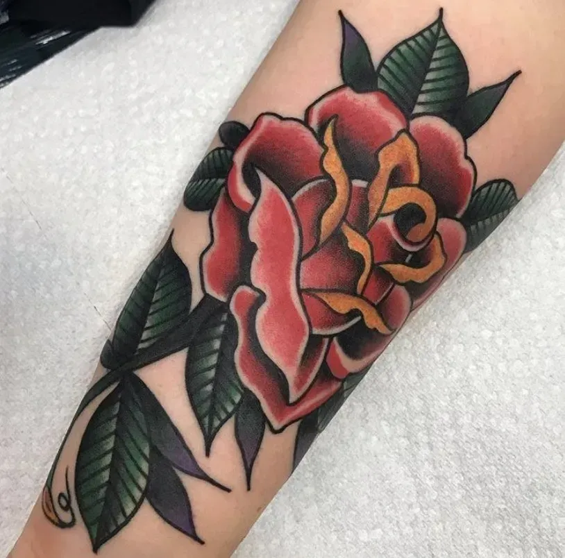 A tattoo of a red rose with green leaves