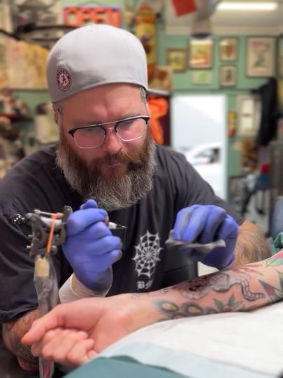 A man with a beard is getting a tattoo on a person 's arm.