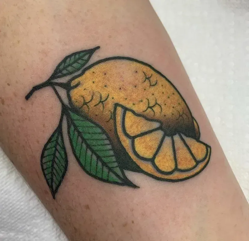A tattoo of an orange with leaves on a person 's arm.