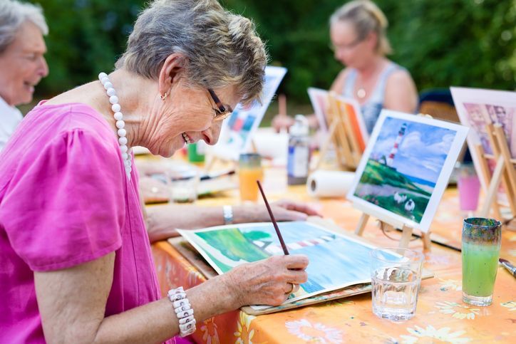 Una donna anziana è seduta a un tavolo e dipinge un quadro.