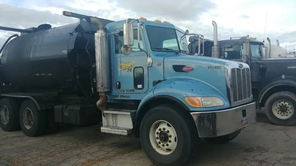 Blue Peterbilt truck with black tank, parked outdoors.
