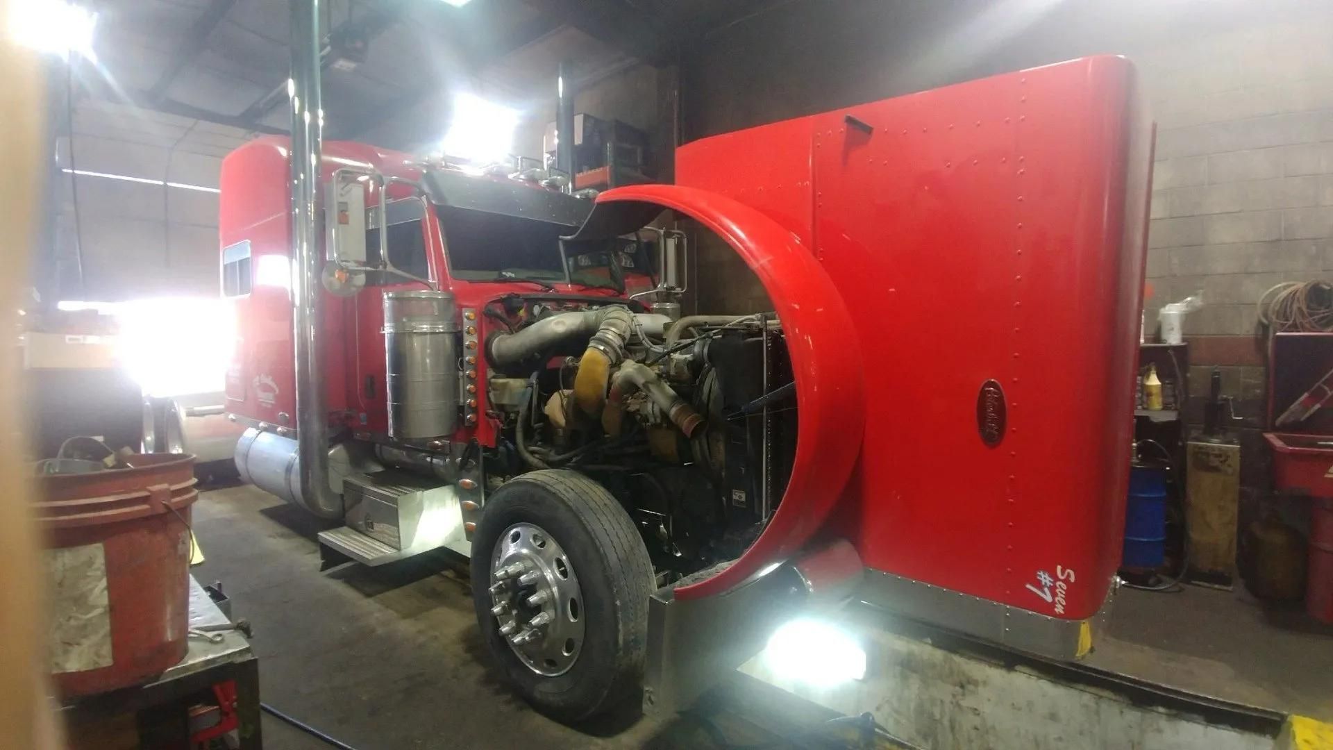 Red semi-truck with hood open in a repair shop.
