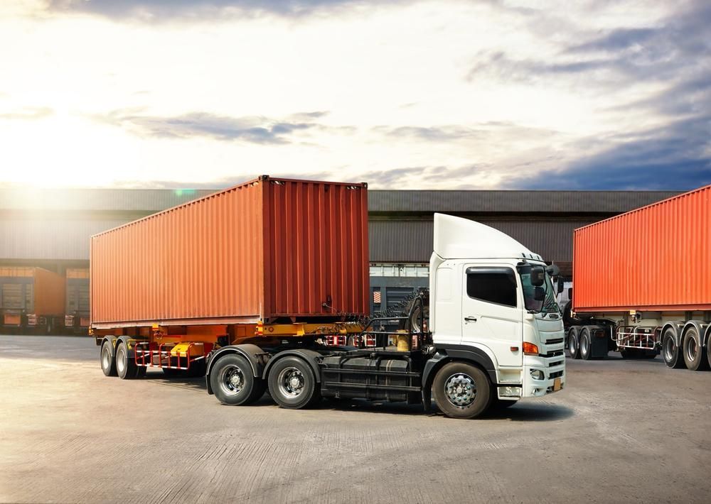 White semi-truck with orange cargo container parked near a loading dock under a cloudy sky.