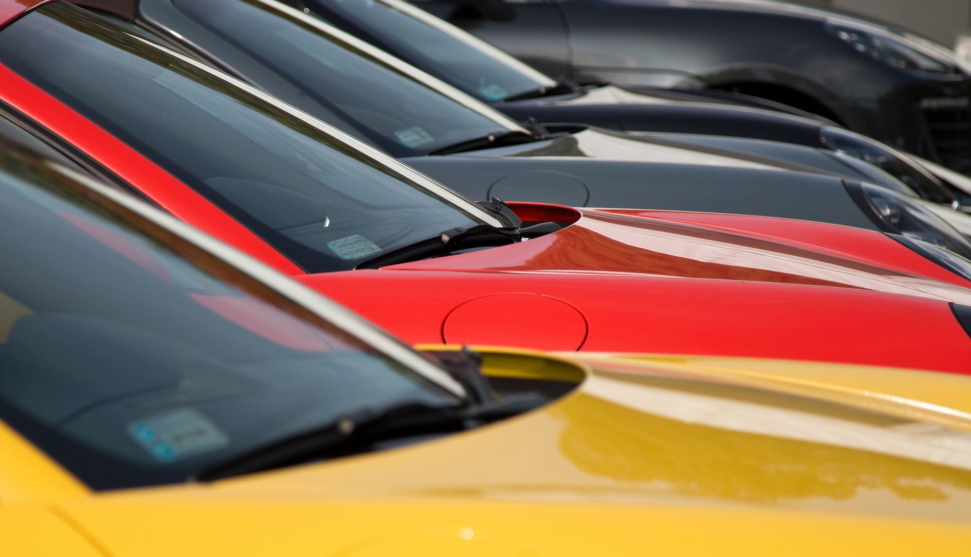 Rows of parked colorful cars lined up closely, showing windshields and hoods in a lot.