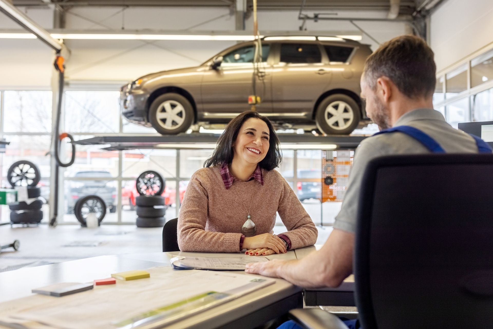 Woman smiling at mechanic in auto shop, car on lift above them.
