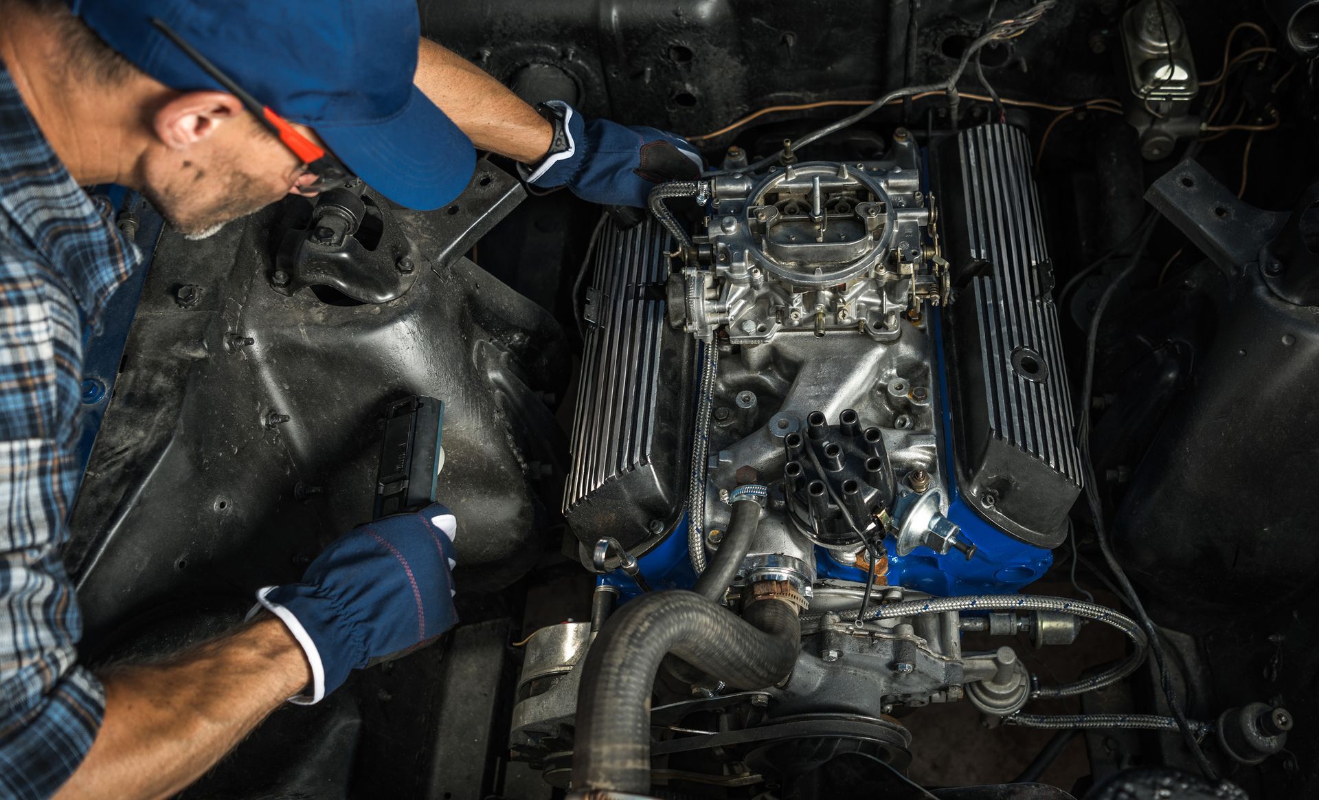 A man with gloves & glasses repairing an engine of a car, showcasing skills in Porsche auto repair.