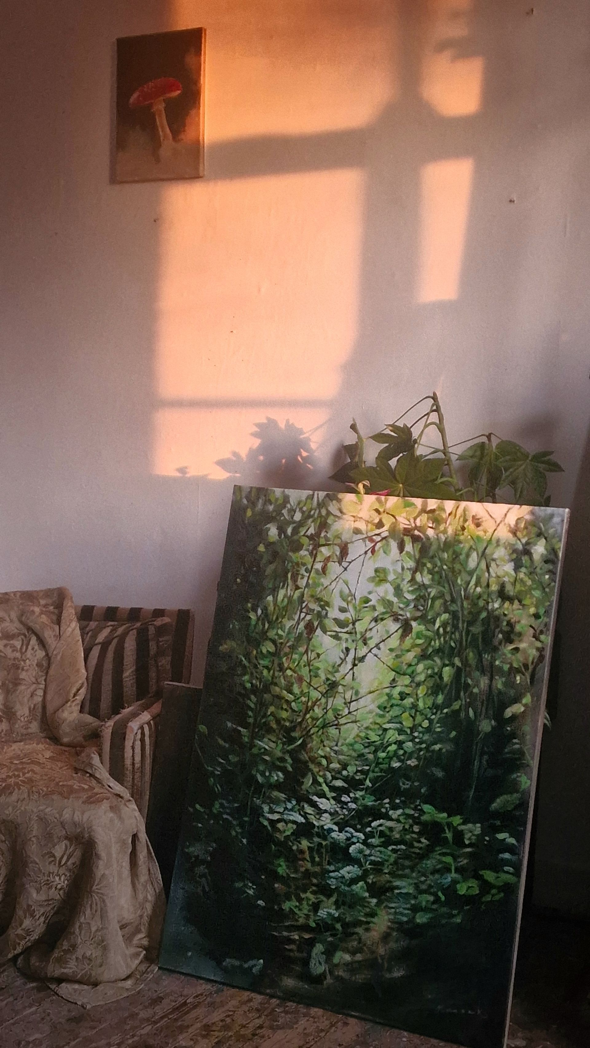 Een zonnige kamer met een groot schilderij van een bos dat tegen de muur leunt, naast een bank en potplanten.