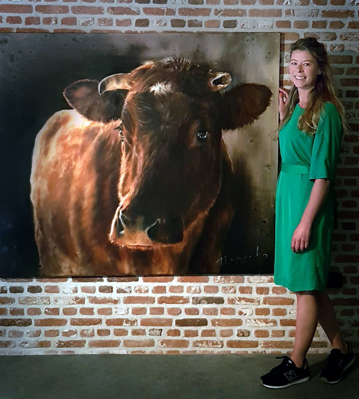 Een vrouw in een groene jurk staat voor een groot schilderij van een koe
