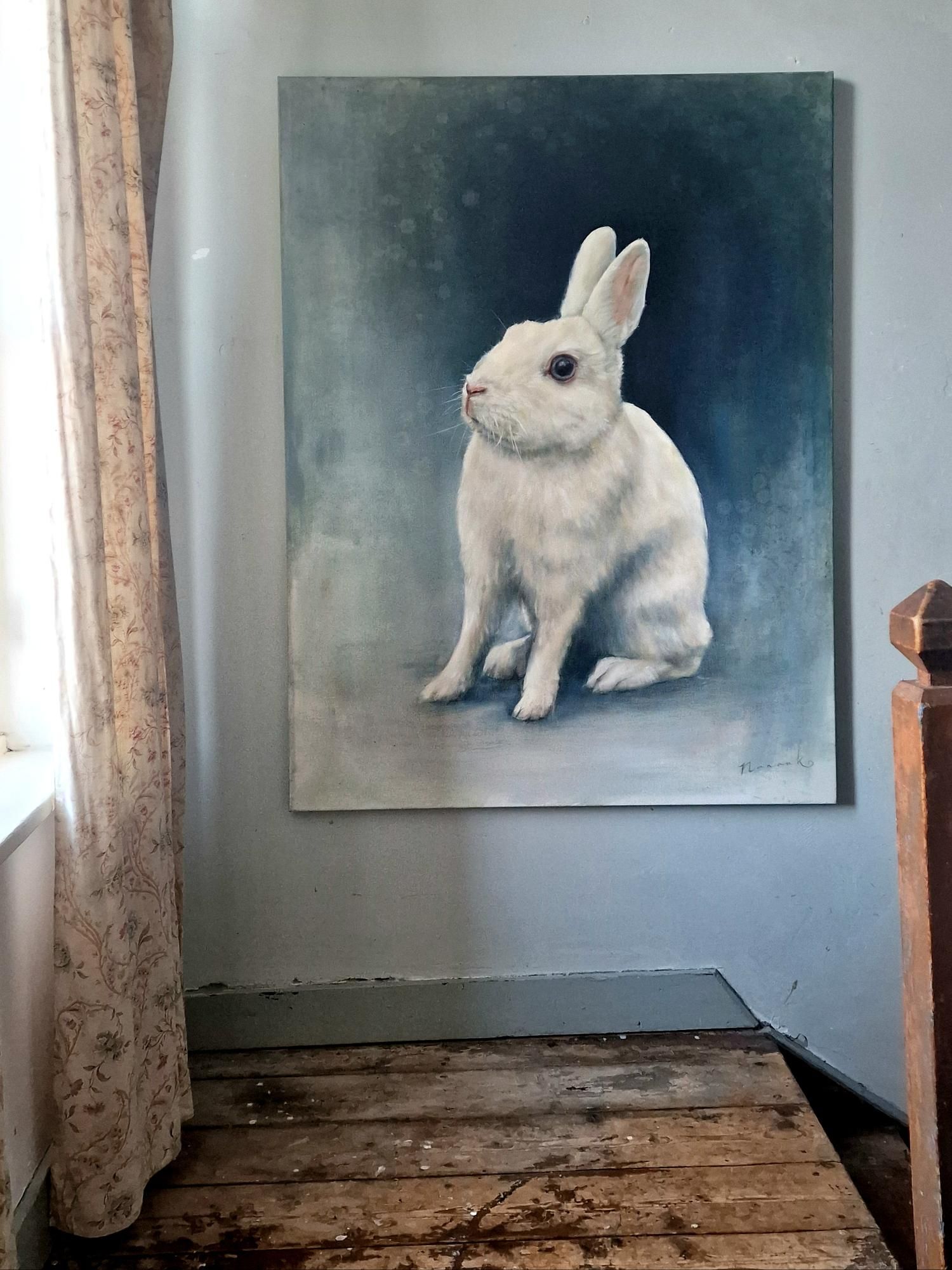 Een schilderij van een wit konijn hangt aan de muur van een kamer.