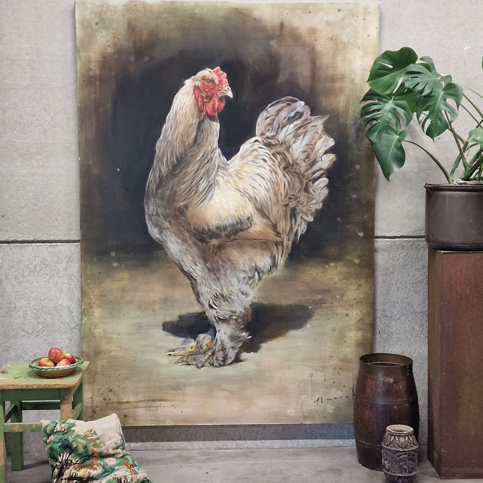 Een geschilderde haan op een doek naast een potplant en kleine decoratieve voorwerpen.