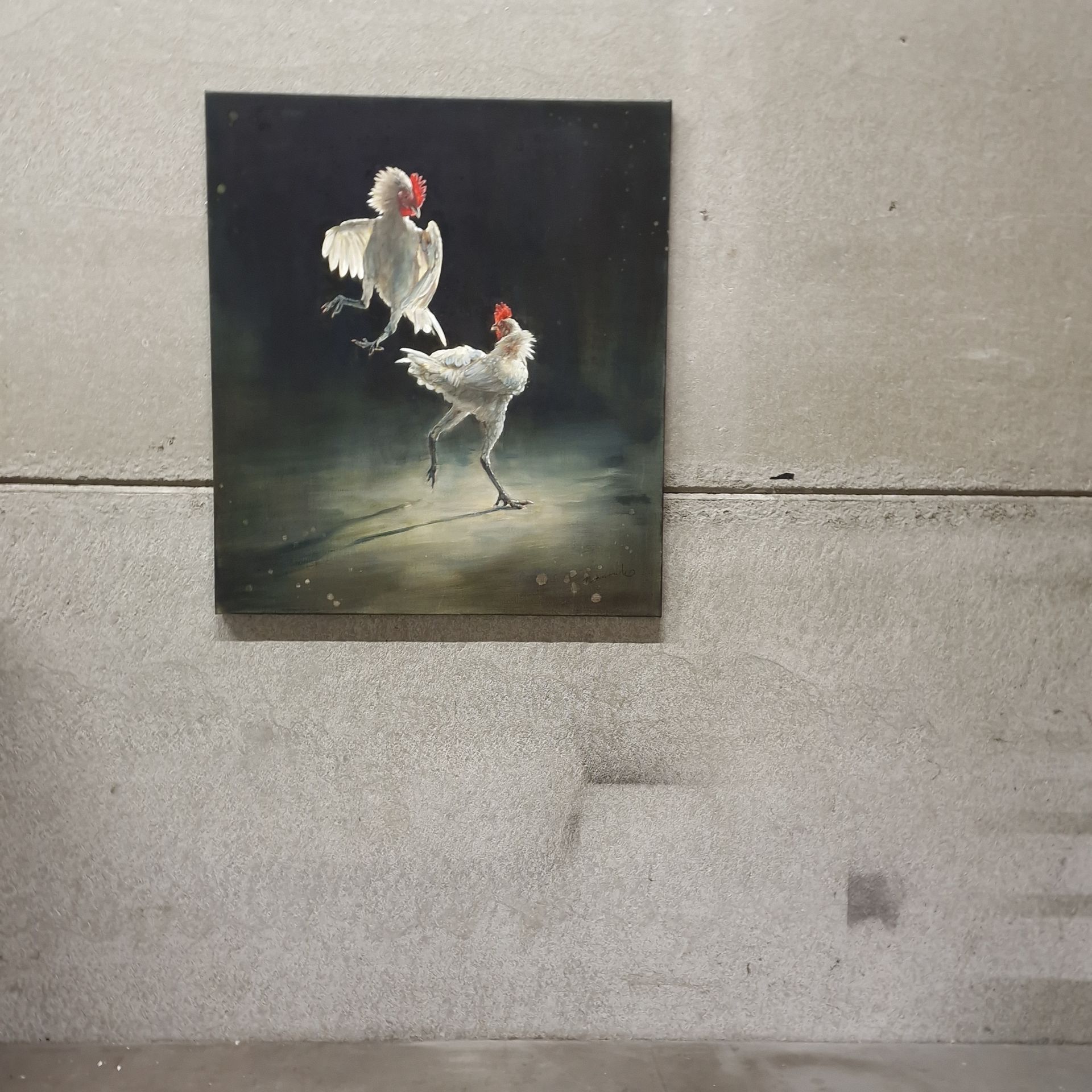 Twee witte hanen met rode kammen op een donker schilderij, dat aan een grijze betonnen muur hangt.