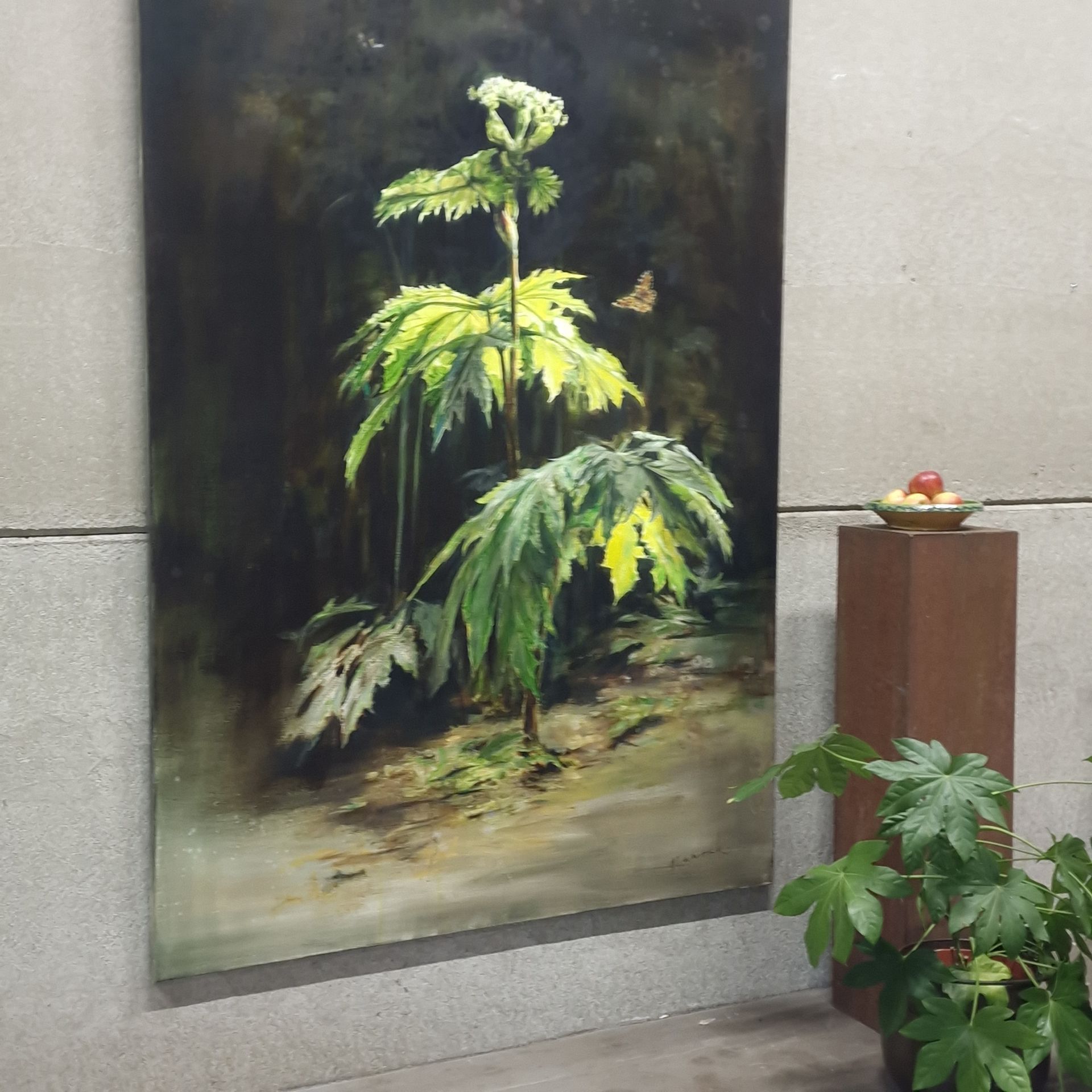 Schilderij van een groene plant met weelderig blad op een donkere muur, naast een klein voetstuk met fruit en een potplant.
