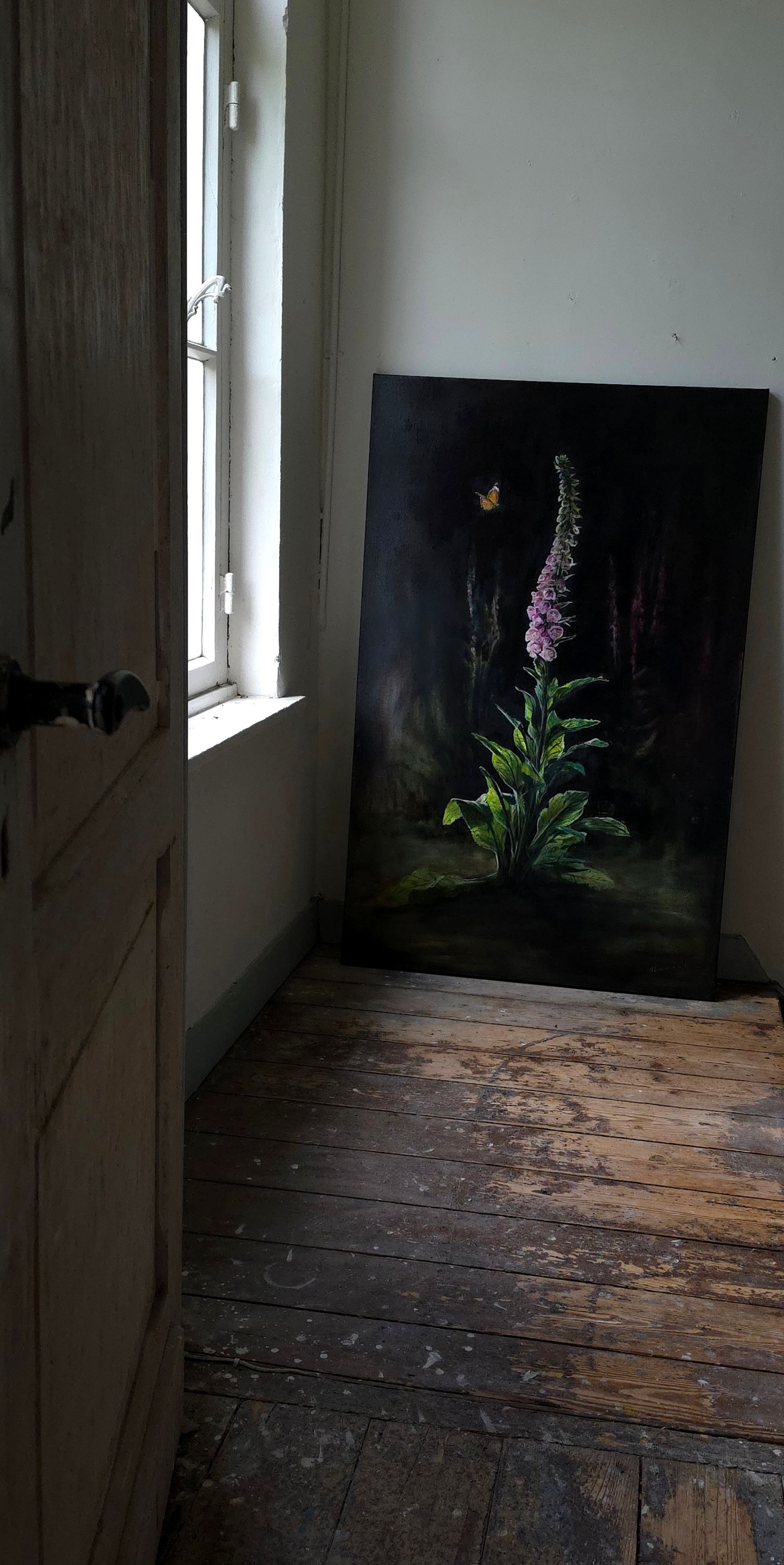 Een schemerige gang met een ingelijst bloemenschilderij dat tegen de muur bij een raam leunt.