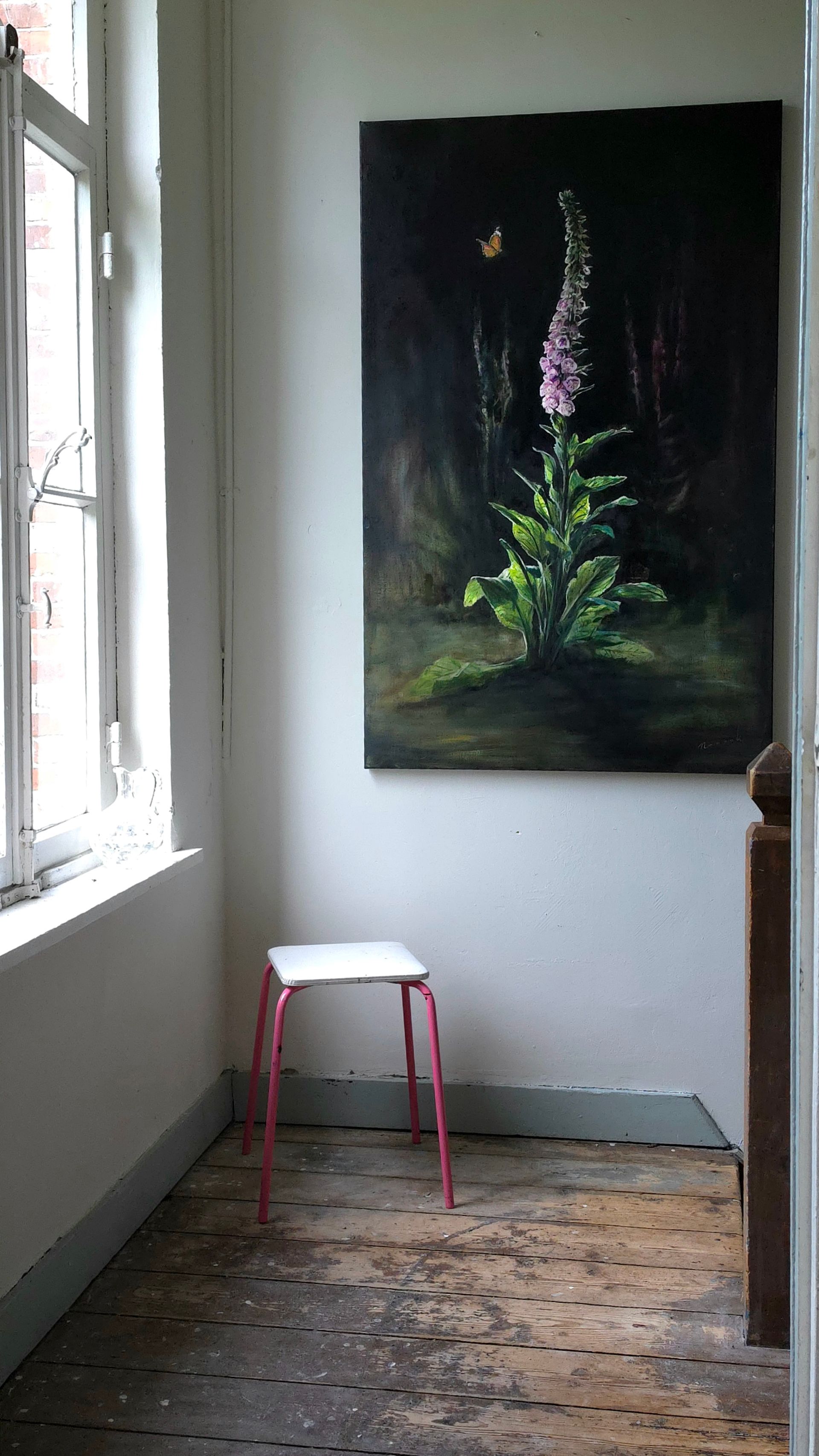Een klein wit krukje met roze poten in een smalle kamer naast een raam, met aan de muur een donker bloemenschilderij.