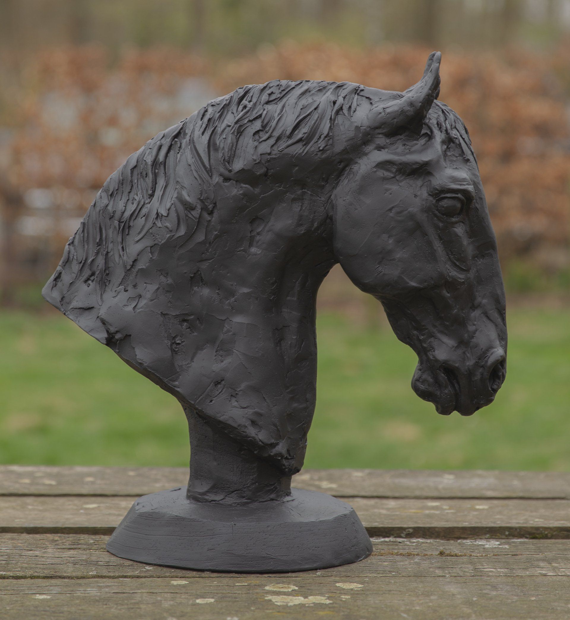 Een zwart beeld van een paardenhoofd staat op een houten tafel.