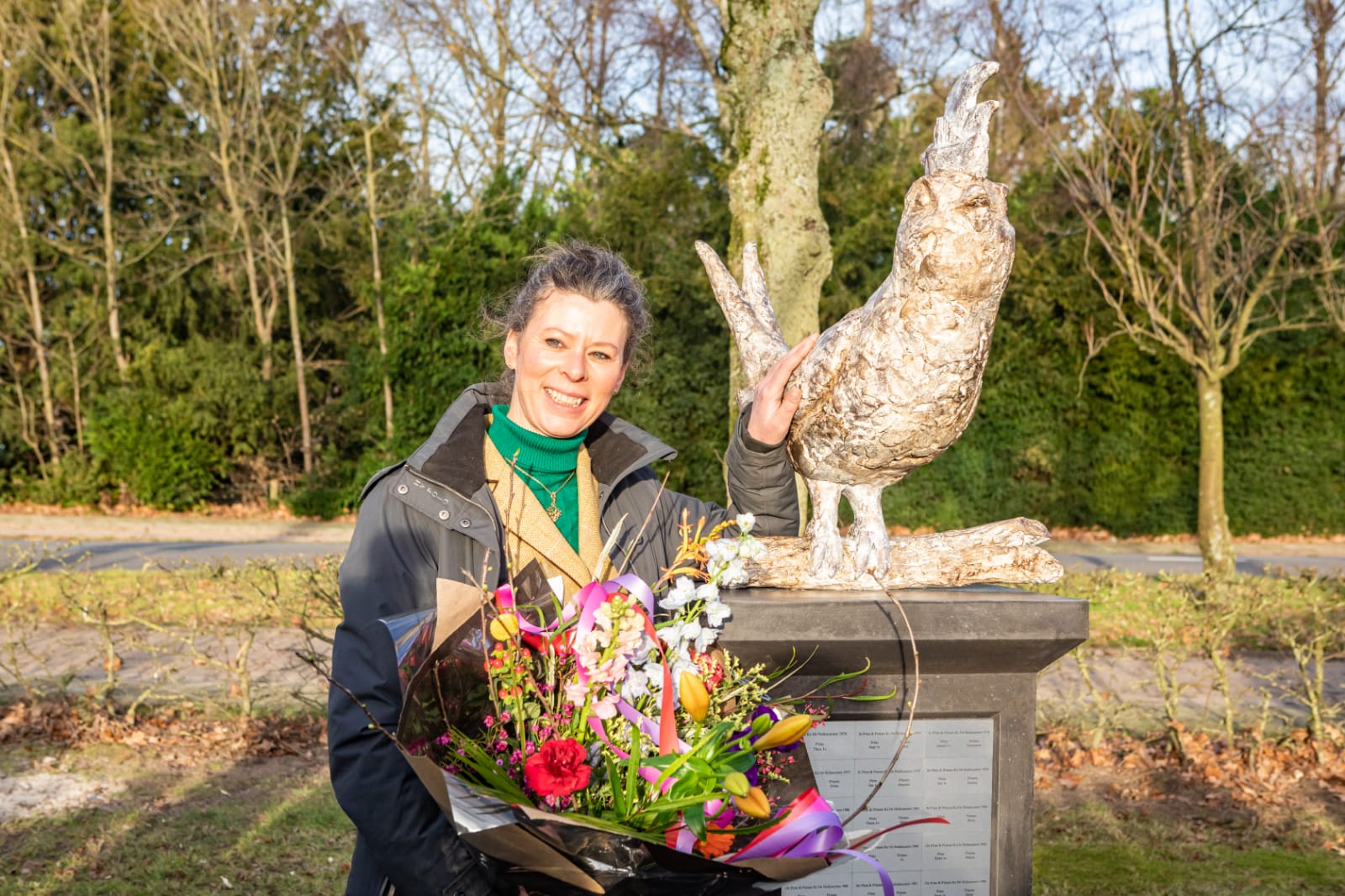 Een vrouw houdt een boeket bloemen vast voor een beeld van een uil.