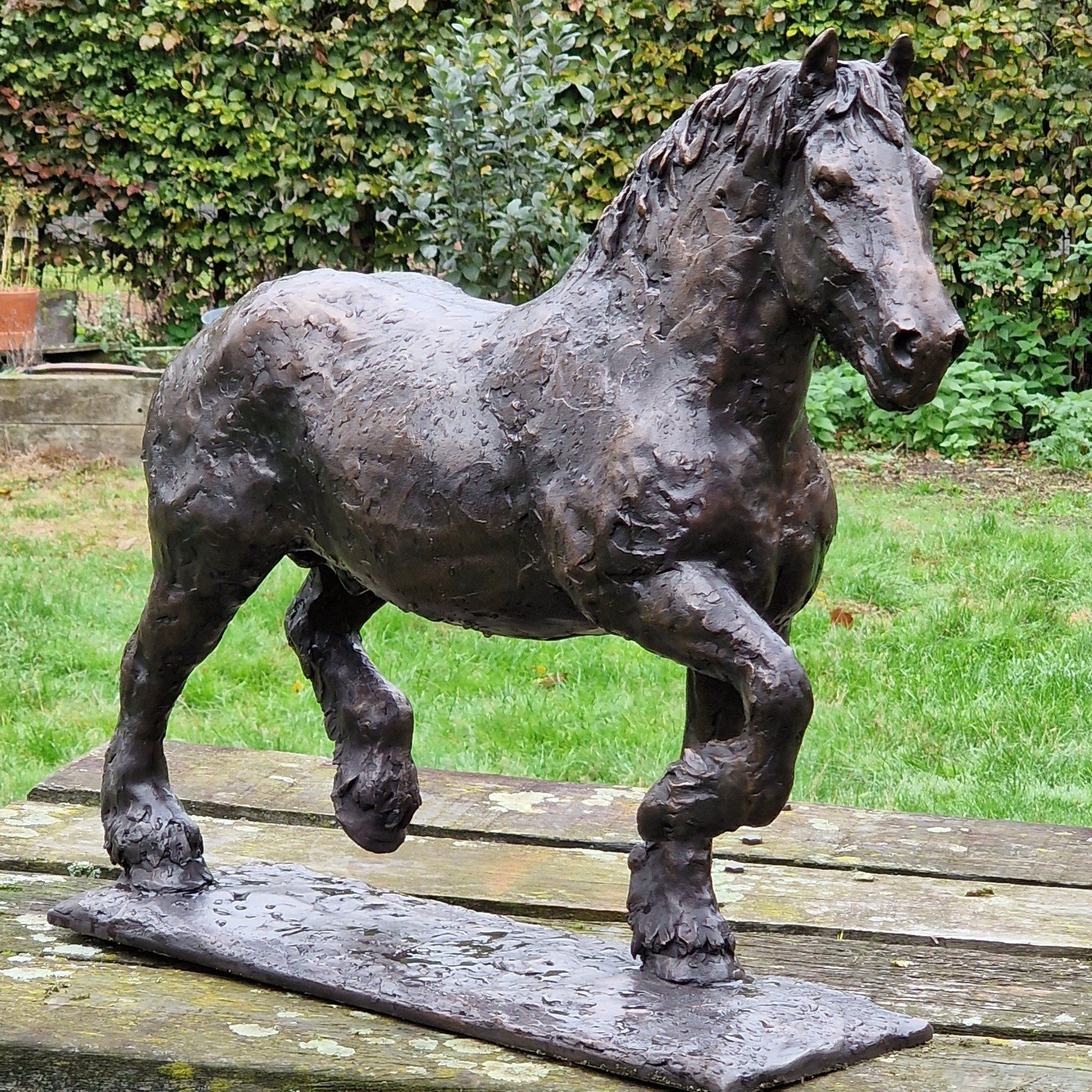 Op een houten tafel staat een bronzen beeld van een paard.