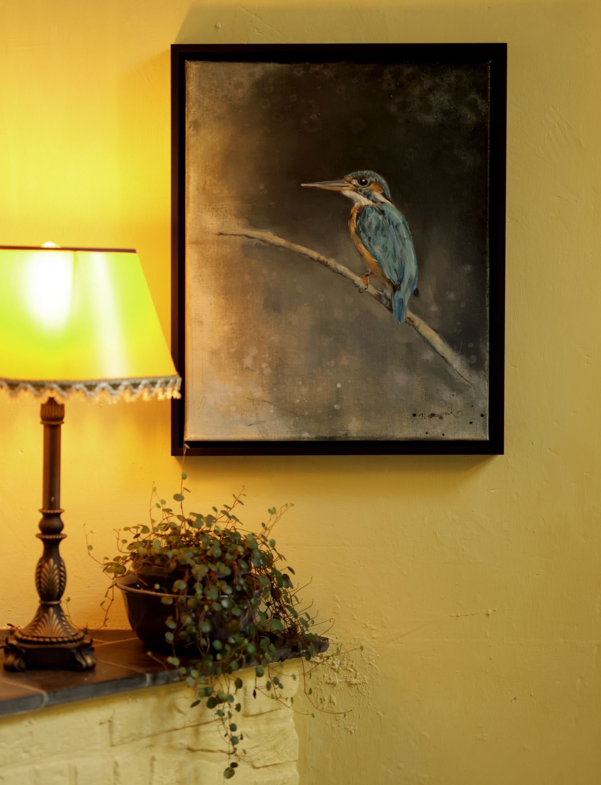 Een schilderij van een vogel die aan een muur hangt naast een lamp