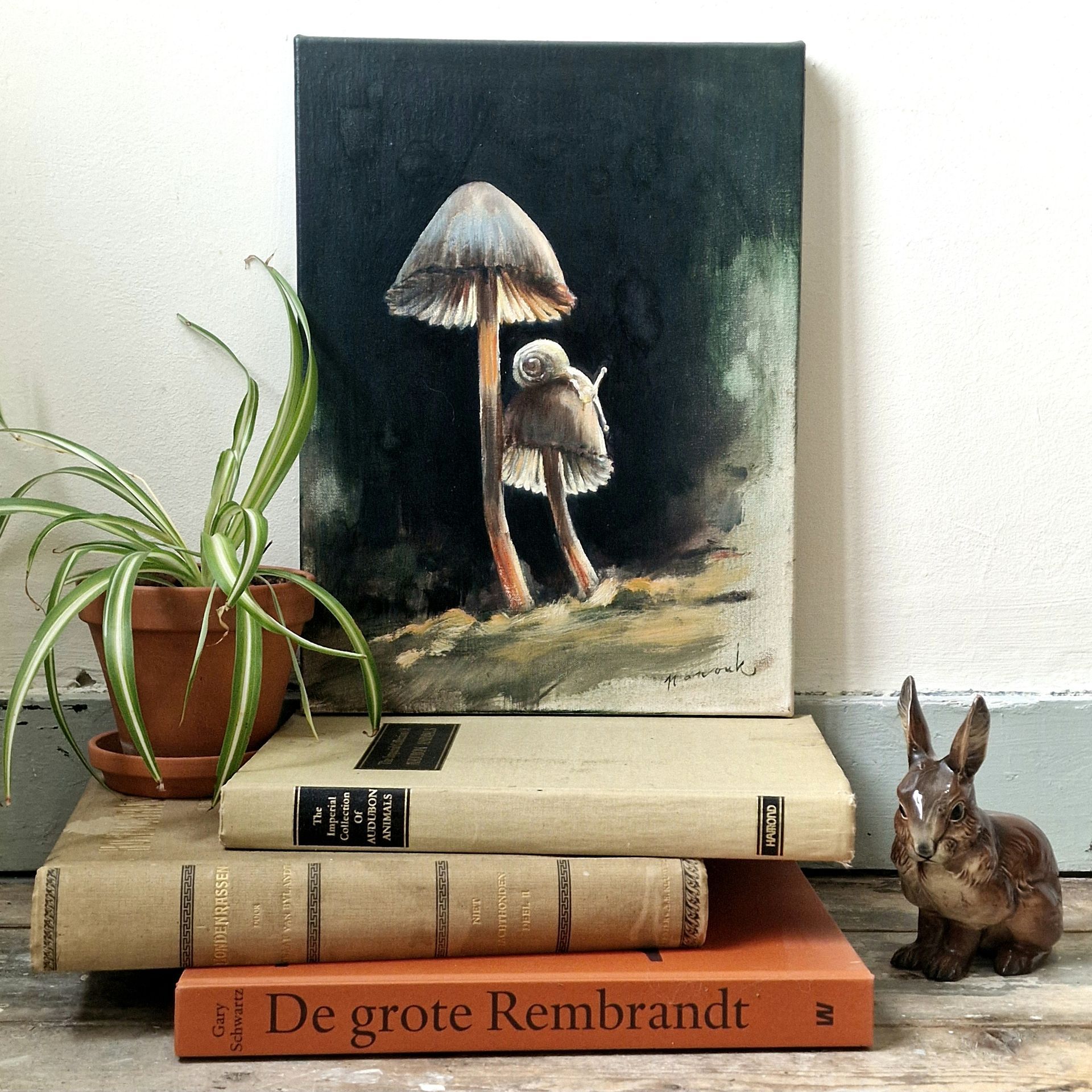 Stilleven met een paddenstoelenschilderij, boeken, een plant en een keramisch konijn.