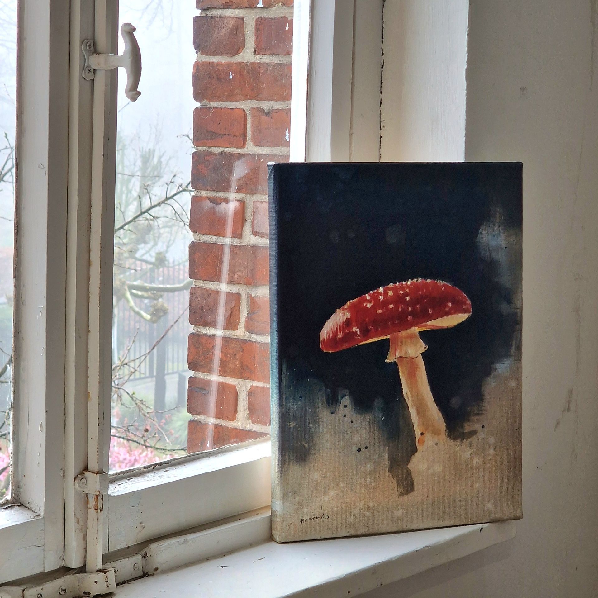 Schilderij van een rode paddenstoel met witte vlekken; staat op een vensterbank, met een bakstenen muur op de achtergrond.