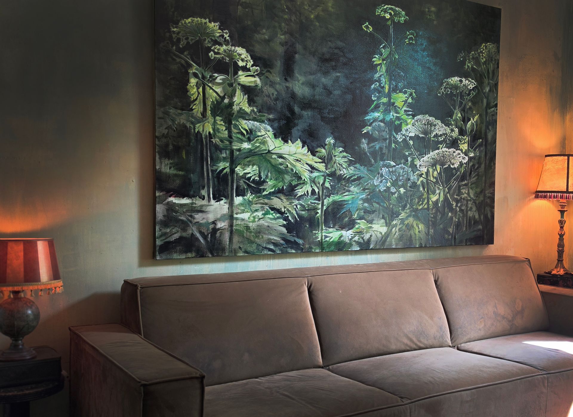 Woonkamer met bruine bank, muurdecoratie met bosmotief en warme lampen aan weerszijden.