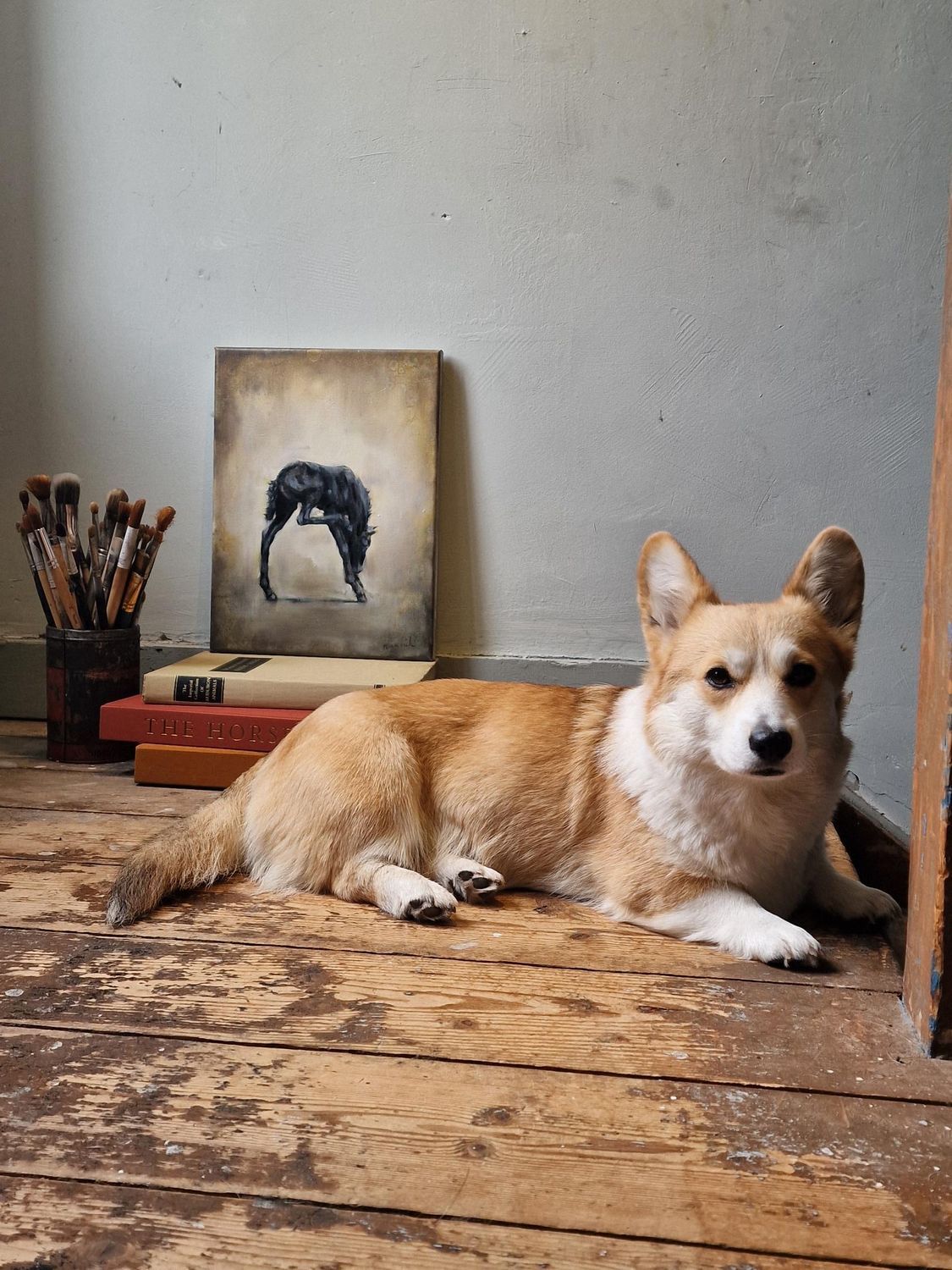 Een hond ligt op een houten vloer voor een schilderij.